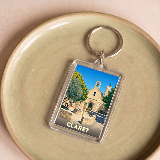 Porte-clés souvenir de la ville de Claret avec une illustration stylisée de son église et de sa place.