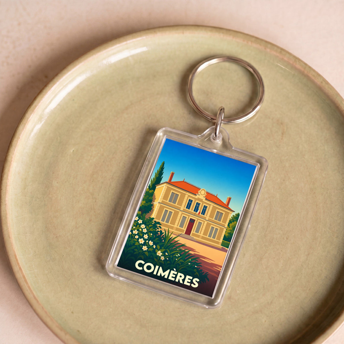 Porte-clés souvenir de la ville de Coimères avec une illustration stylisée d'une bâtisse.