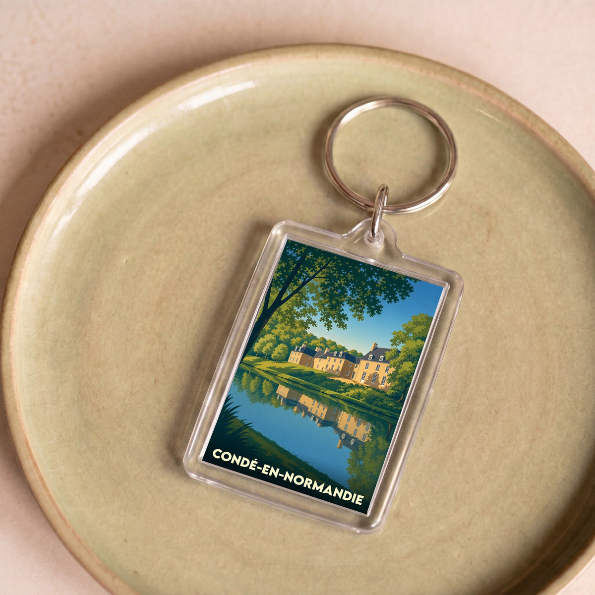 Porte-clés souvenir de la ville de Condé-en-Normandie avec une illustration stylisée d'un manoir se reflétant dans l'eau.