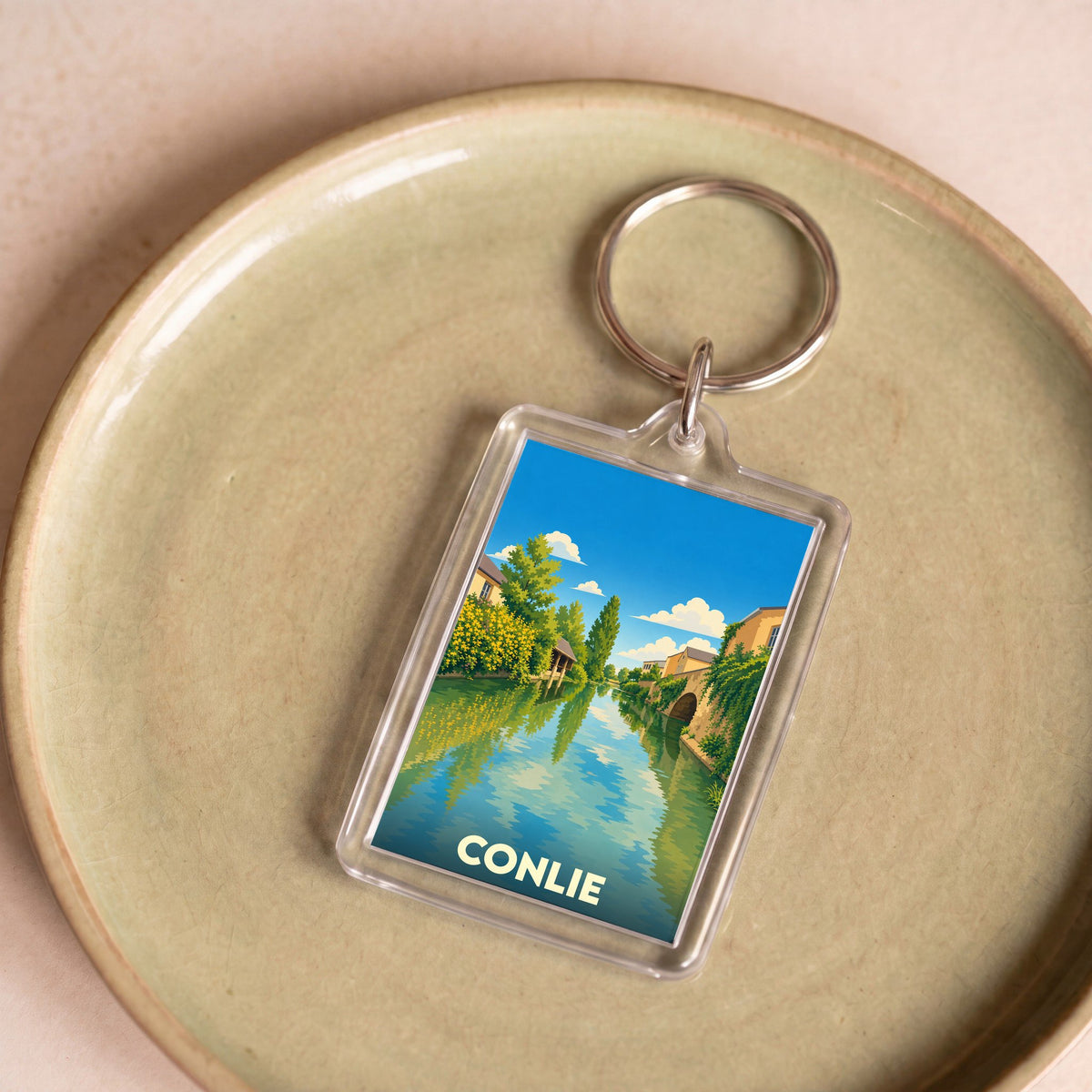Porte-clés souvenir de la ville de Conlie avec une illustration stylisée d'un canal bordé de maisons.