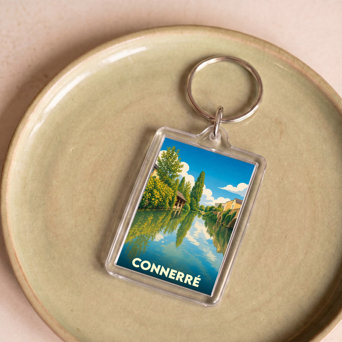 Porte-clés souvenir de la ville de Connerré avec une illustration stylisée d'un paysage de bord de rivière.