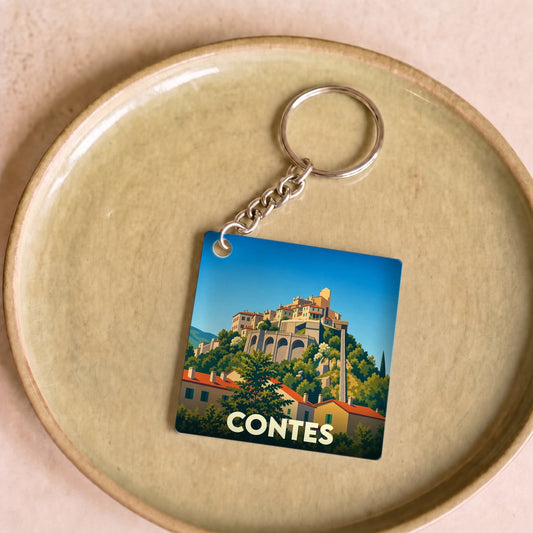 Porte-clés souvenir de la ville de Contes avec une illustration stylisée d'un village perché.