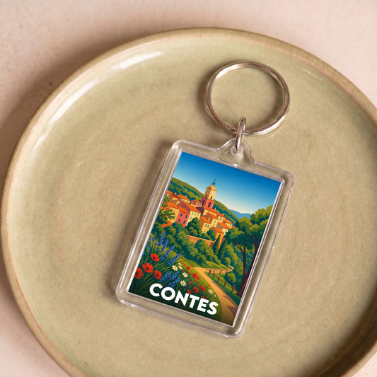 Porte-clés souvenir de la ville de Contes avec une illustration stylisée d'un village perché.