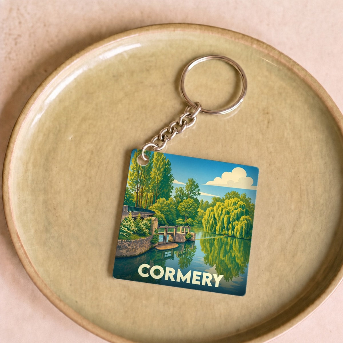 Porte-clés souvenir de la ville de Cormery avec une illustration stylisée d'un paysage de rivière.