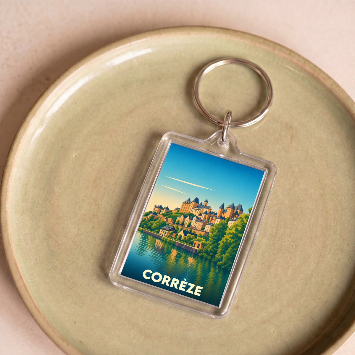 Porte-clés souvenir de la ville de Corrèze avec une illustration stylisée d'un village en bord d'eau.