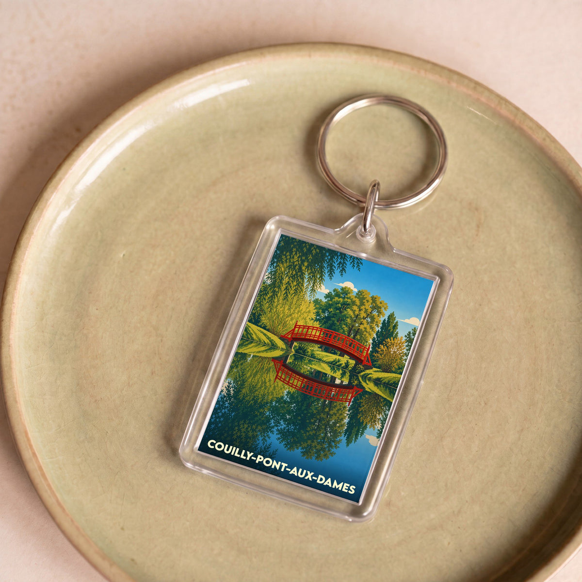 Porte-clés souvenir de la ville de Couilly-Pont-aux-Dames avec une illustration stylisée d'un pont rouge se reflétant dans l'eau.