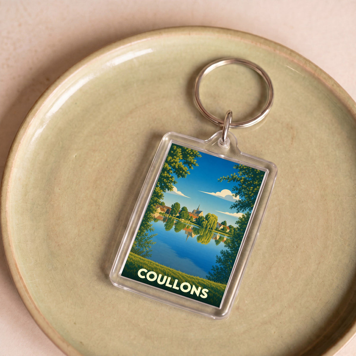 Porte-clés souvenir de la ville de Coullons avec une illustration stylisée d'un paysage au bord de l'eau.