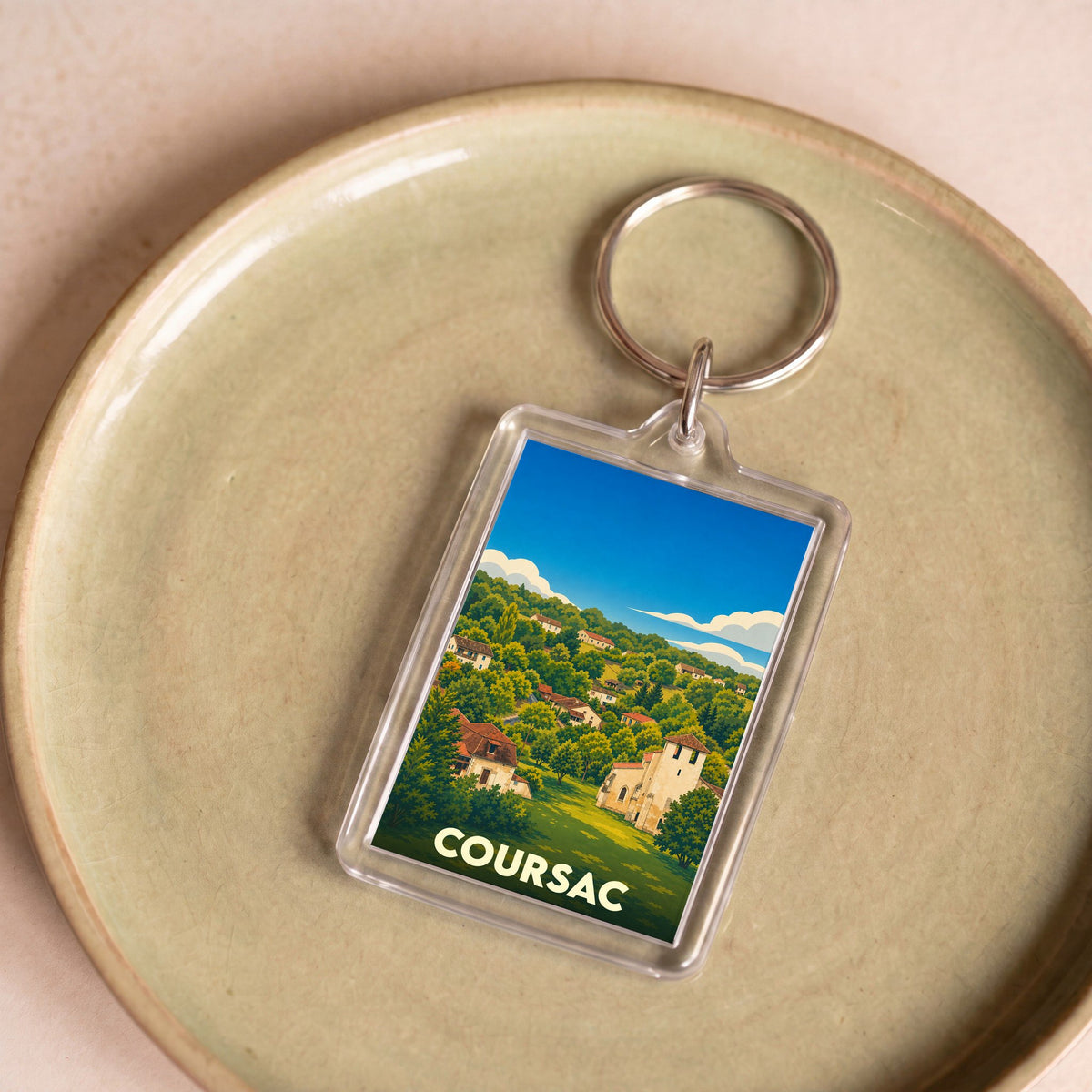 Porte-clés souvenir de la ville de Coursac avec une illustration stylisée de son paysage et de ses maisons.