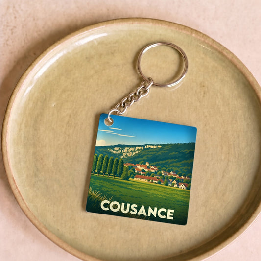 Porte-clés souvenir de la ville de Cousance avec une illustration stylisée de son paysage et de ses habitations.