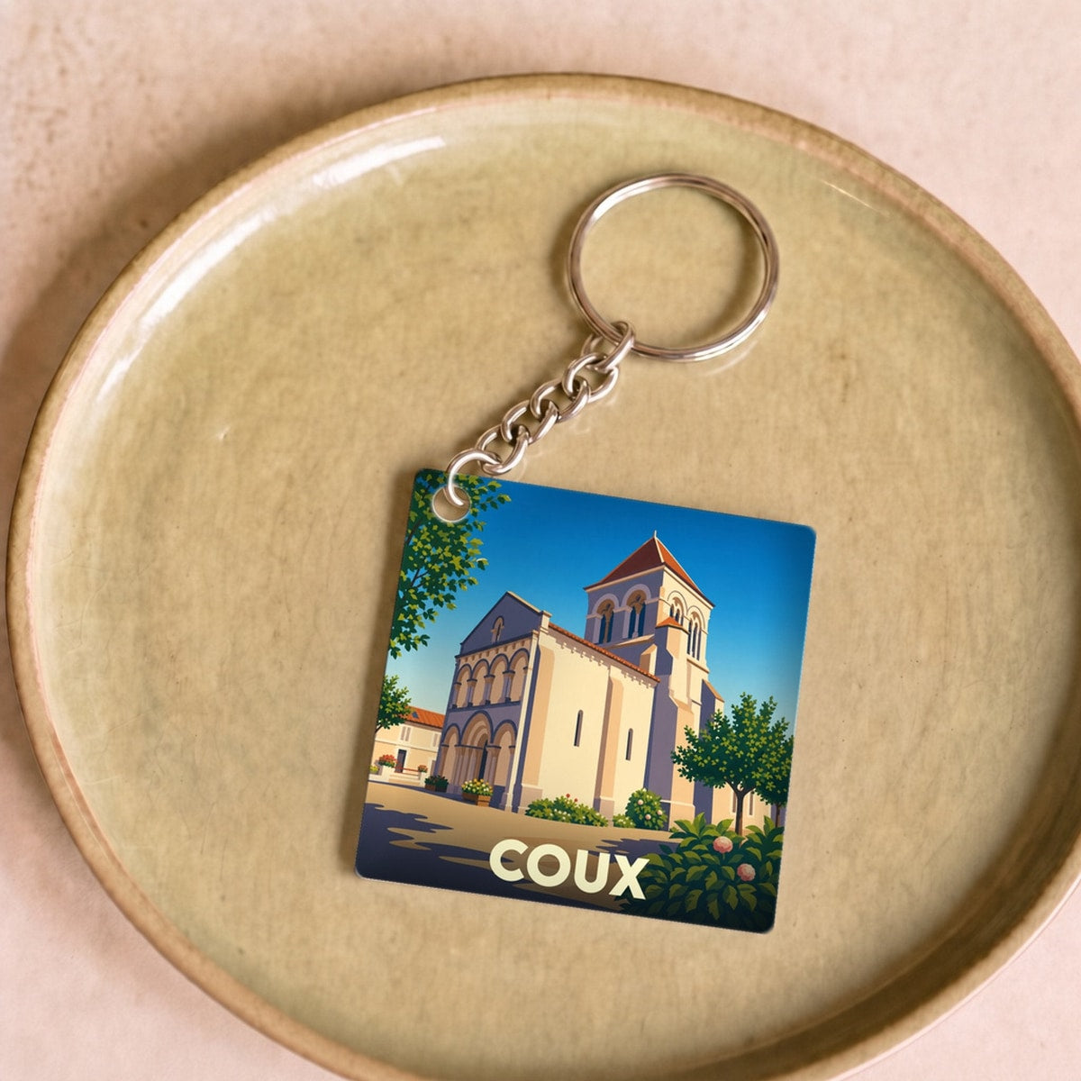 Porte-clés souvenir de la ville de Coux avec une illustration stylisée d'une église sous un ciel bleu.