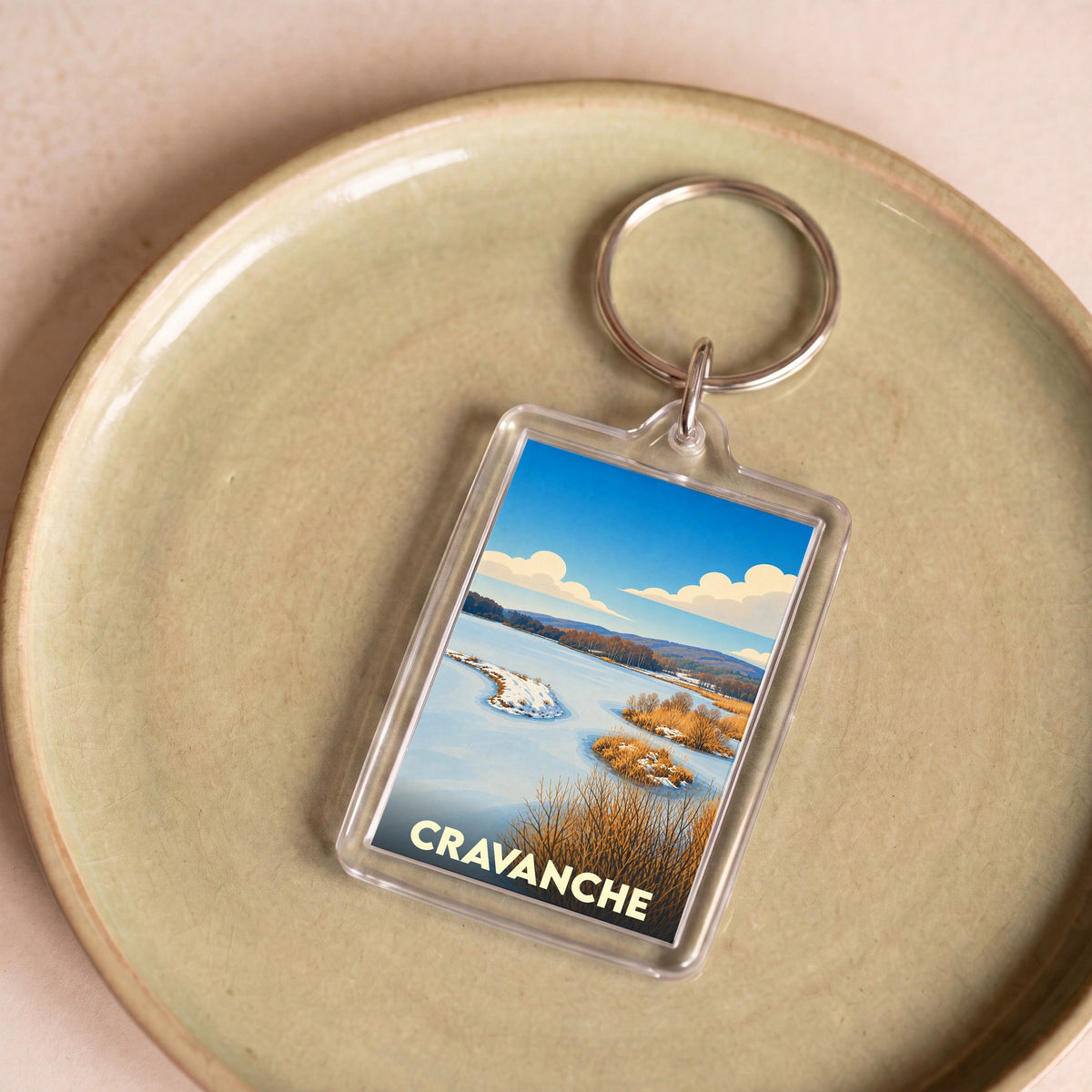 Porte-clés souvenir de la ville de Cravanche avec une illustration stylisée de paysage hivernal.