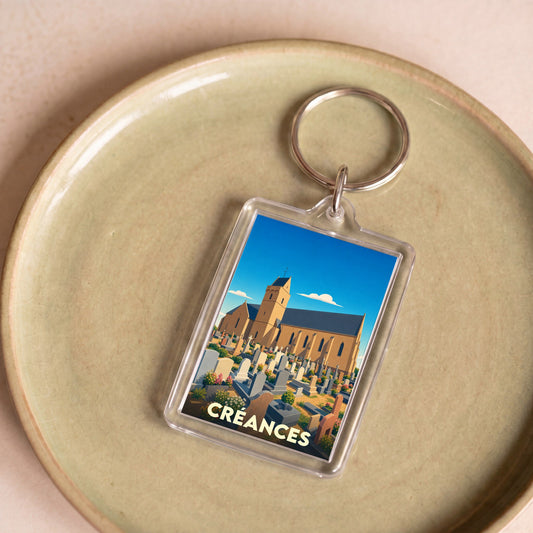 Porte-clés souvenir de la ville de Créances avec une illustration stylisée de son église et de son cimetière.