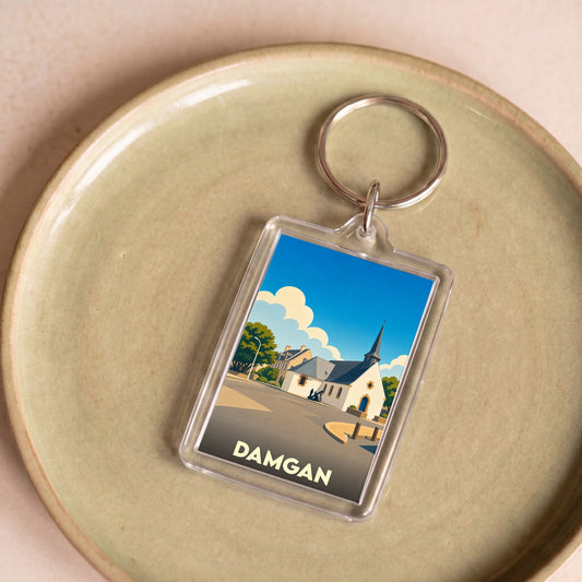 Porte-clés souvenir de la ville de Damgan avec une illustration stylisée de son église sous un ciel bleu.