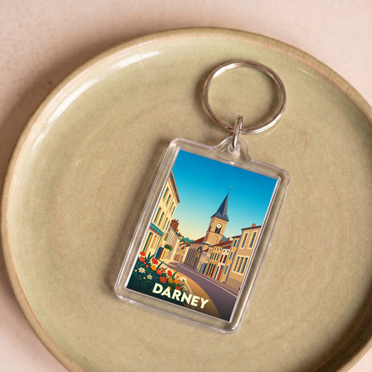 Porte-clés souvenir de la ville de Darney avec une illustration stylisée d'une rue historique.