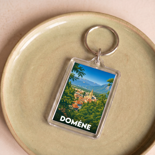Porte-clés souvenir de la ville de Domène avec une illustration stylisée de son paysage urbain et montagneux.
