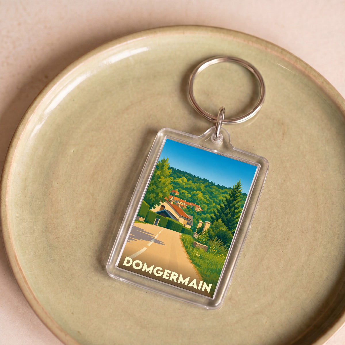 Porte-clés souvenir de la ville de Domgermain avec une illustration stylisée d'un paysage vallonné.