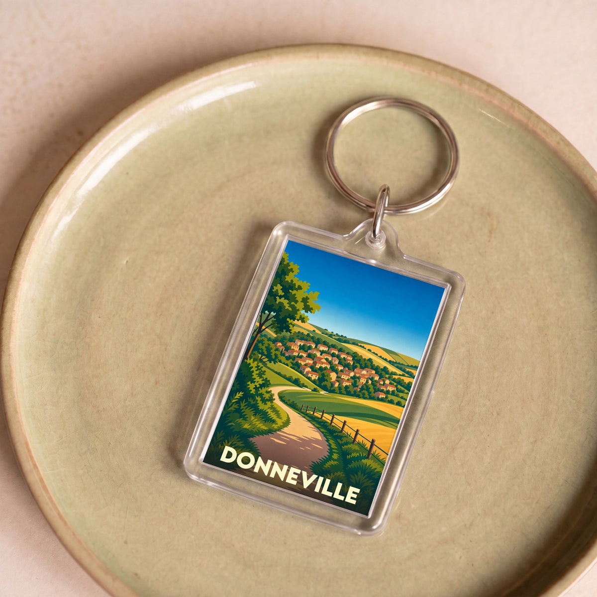 Porte-clés souvenir de la ville de Donneville avec une illustration stylisée de son paysage vallonné.