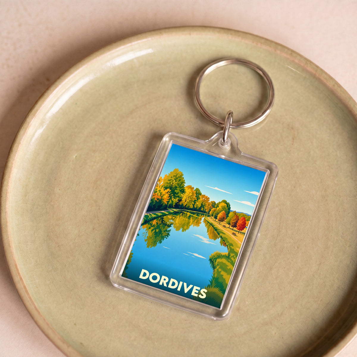 Porte-clés souvenir de la ville de Dordives avec une illustration stylisée d'un paysage automnal au bord de l'eau.