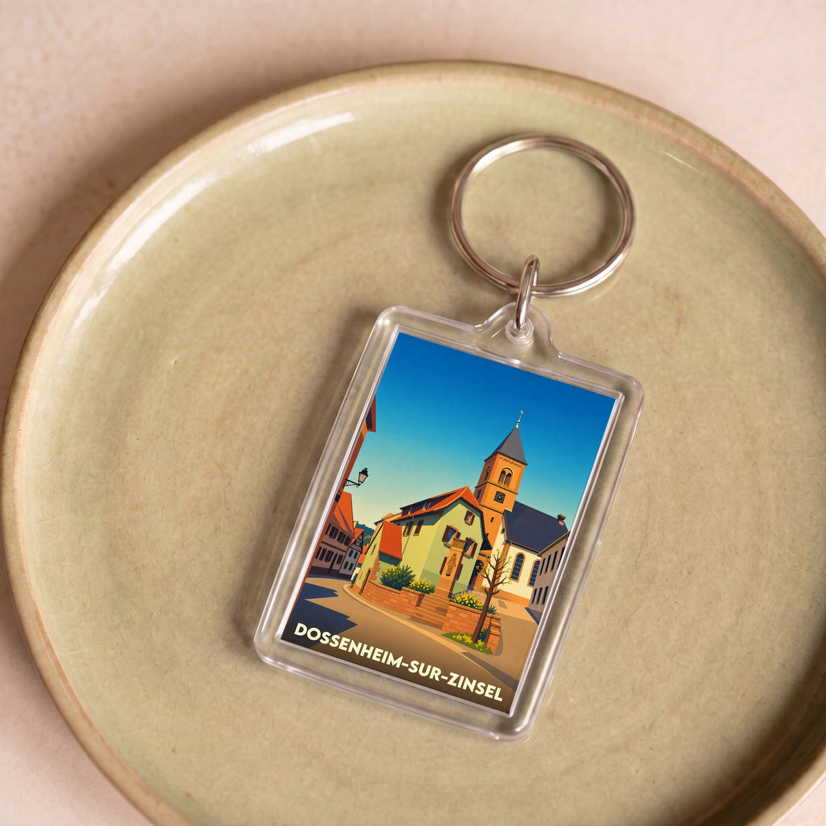 Porte-clés souvenir de la ville de Dossenheim-sur-Zinsel avec une illustration stylisée de son église et de ses maisons alsaciennes.