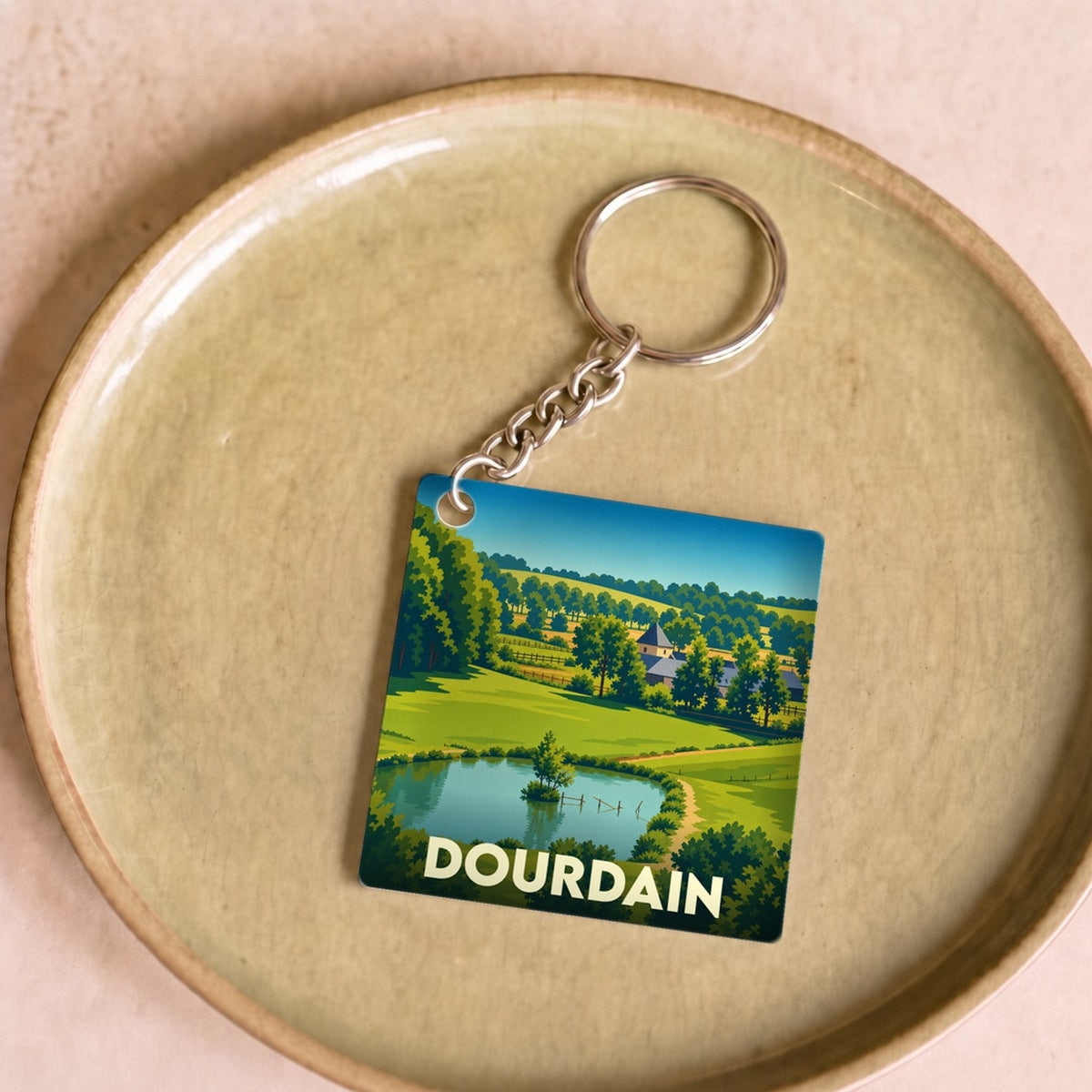 Porte-clés souvenir de la ville de Dourdain avec une illustration de paysage champêtre.