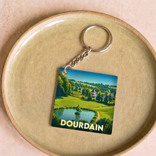 Porte-clés souvenir de la ville de Dourdain avec une illustration de paysage champêtre.