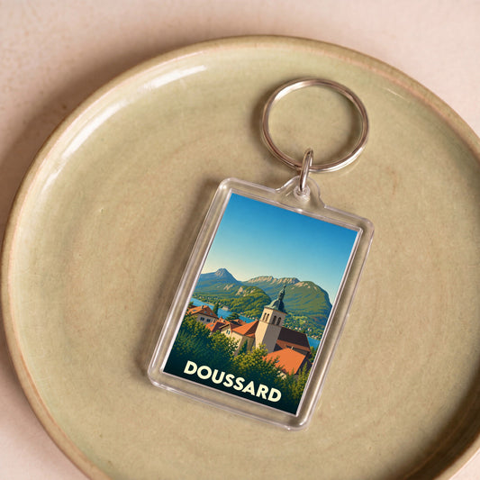 Porte-clés souvenir de la ville de Doussard avec une illustration stylisée de son église et du lac.