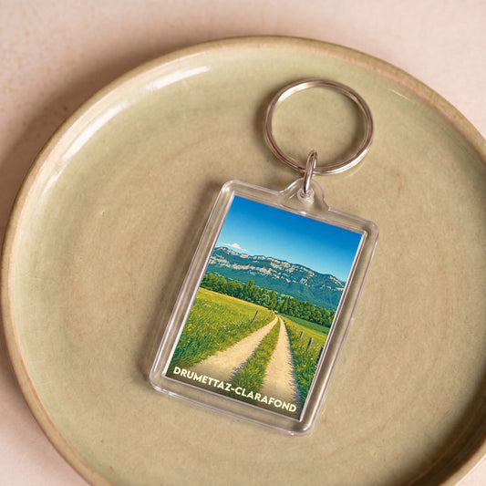 Porte-clés souvenir de la ville de Drumettaz-Clarafond avec une illustration stylisée d'un paysage de campagne.