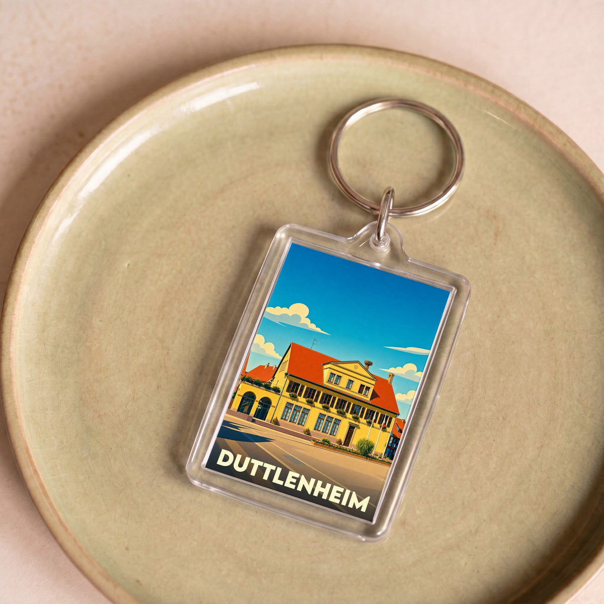 Porte-clés souvenir de la ville de Duttlenheim avec une illustration stylisée d'un bâtiment traditionnel.