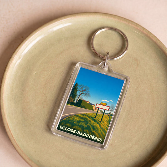 Porte-clés souvenir de la commune d'Eclose-Badinières avec une illustration paysagère stylisée.