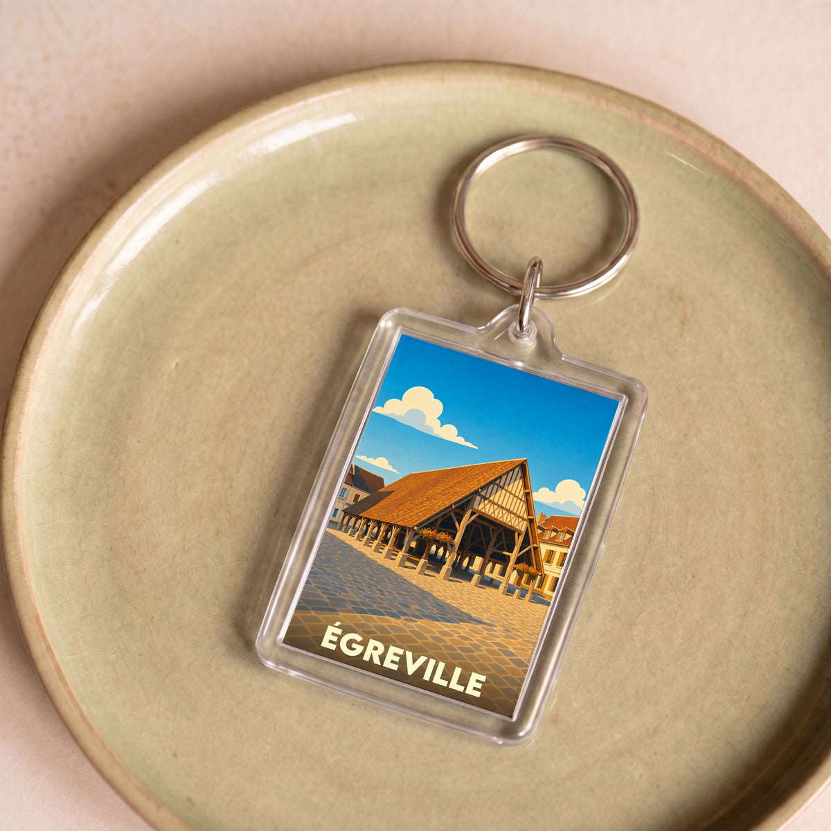 Porte-clés souvenir de la ville de Égreville avec une illustration stylisée de ses halles historiques.