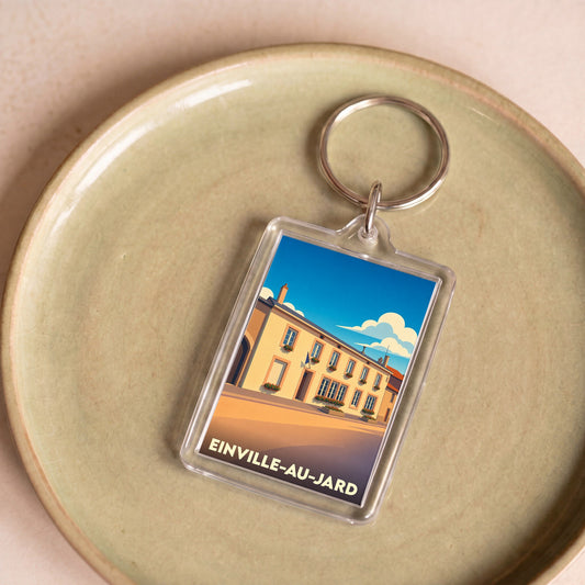 Porte-clés souvenir de la ville de Einville-au-Jard avec une illustration stylisée d'un bâtiment ensoleillé.