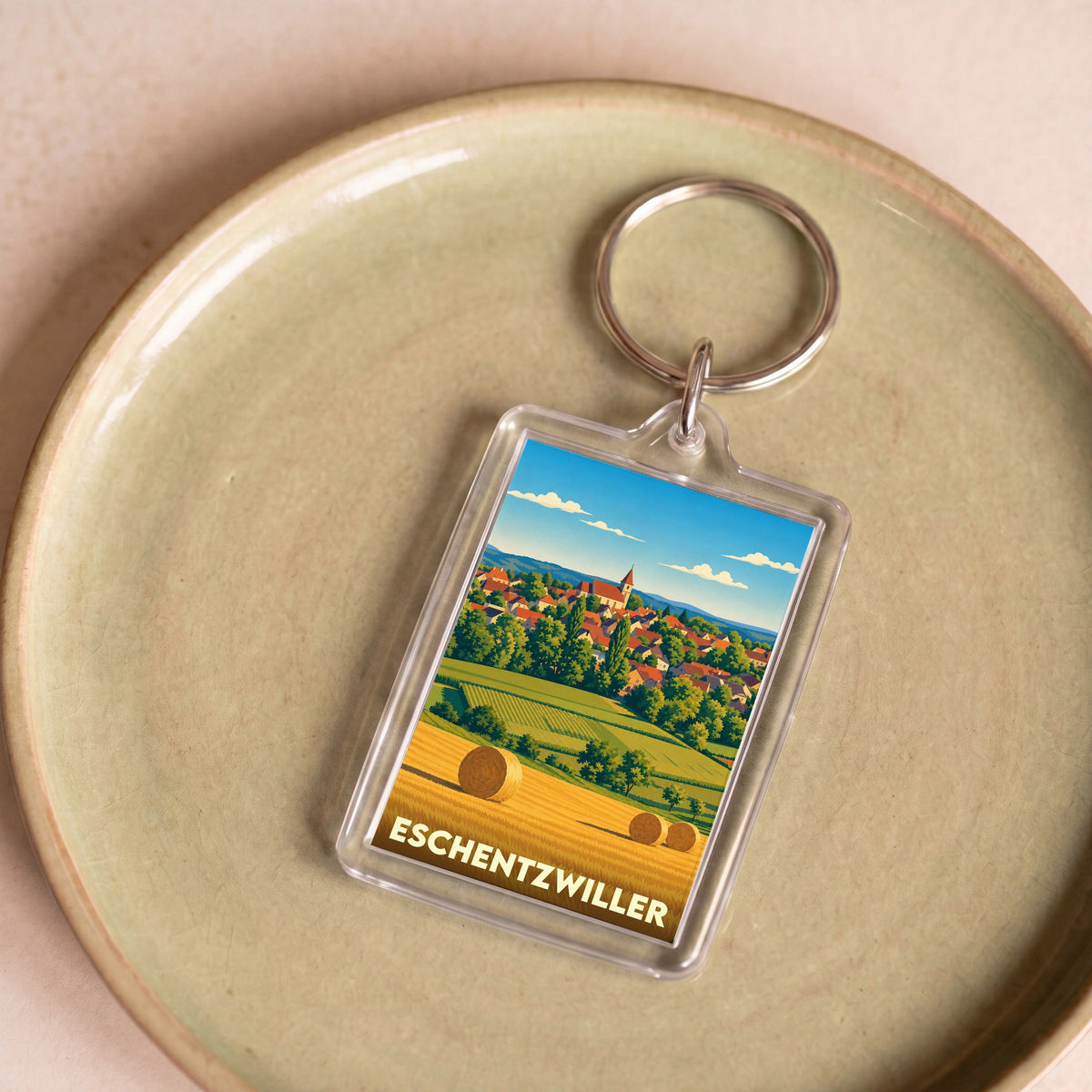 Porte-clés souvenir de la ville de Eschentzwiller avec une illustration stylisée de son paysage rural.