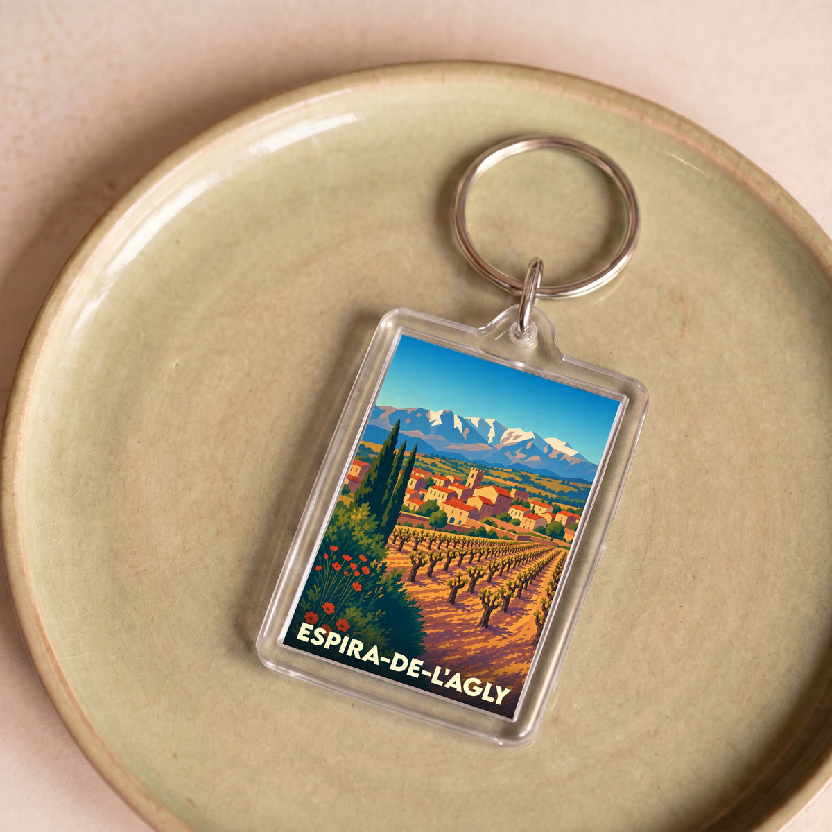 Porte-clés souvenir de la ville d'Espira-de-l'Agly avec une illustration stylisée de ses vignobles et montagnes.