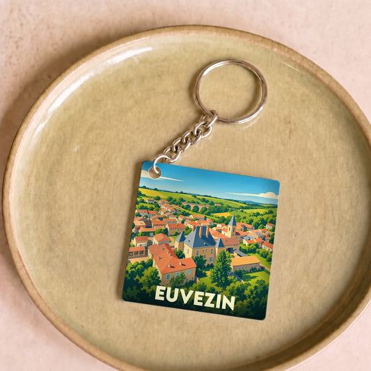 Porte-clés souvenir de la ville d'Euvezin avec une illustration stylisée d'un paysage de village.