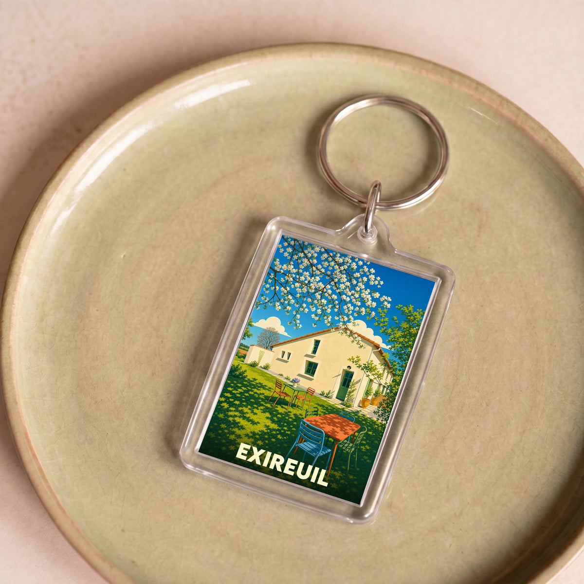 Porte-clés souvenir de la ville de Exireuil avec une illustration stylisée d'une maison de campagne ensoleillée.