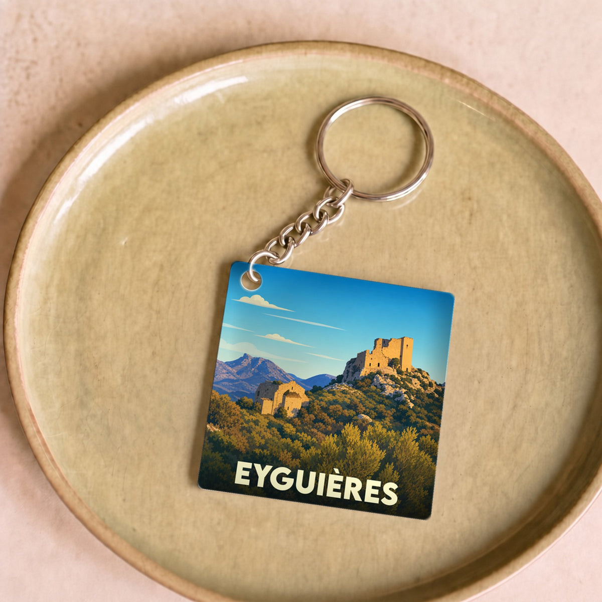 Porte-clés souvenir de la ville de Eyguières avec une illustration stylisée d'un paysage provençal.