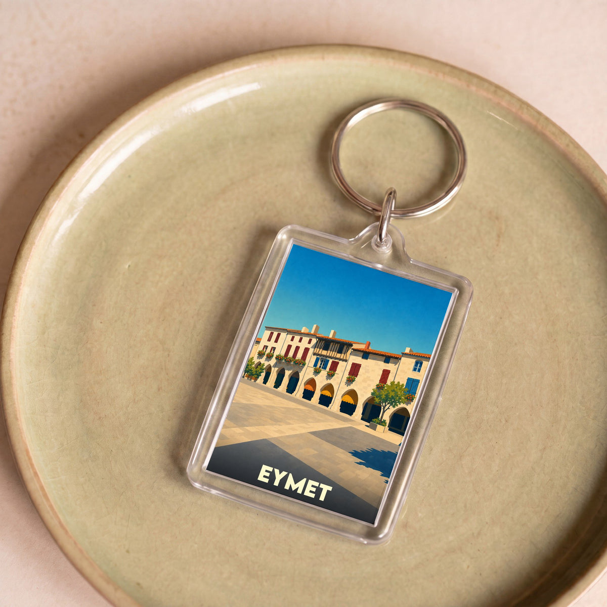Porte-clés souvenir de la ville de Eymet avec une illustration stylisée de sa place centrale.