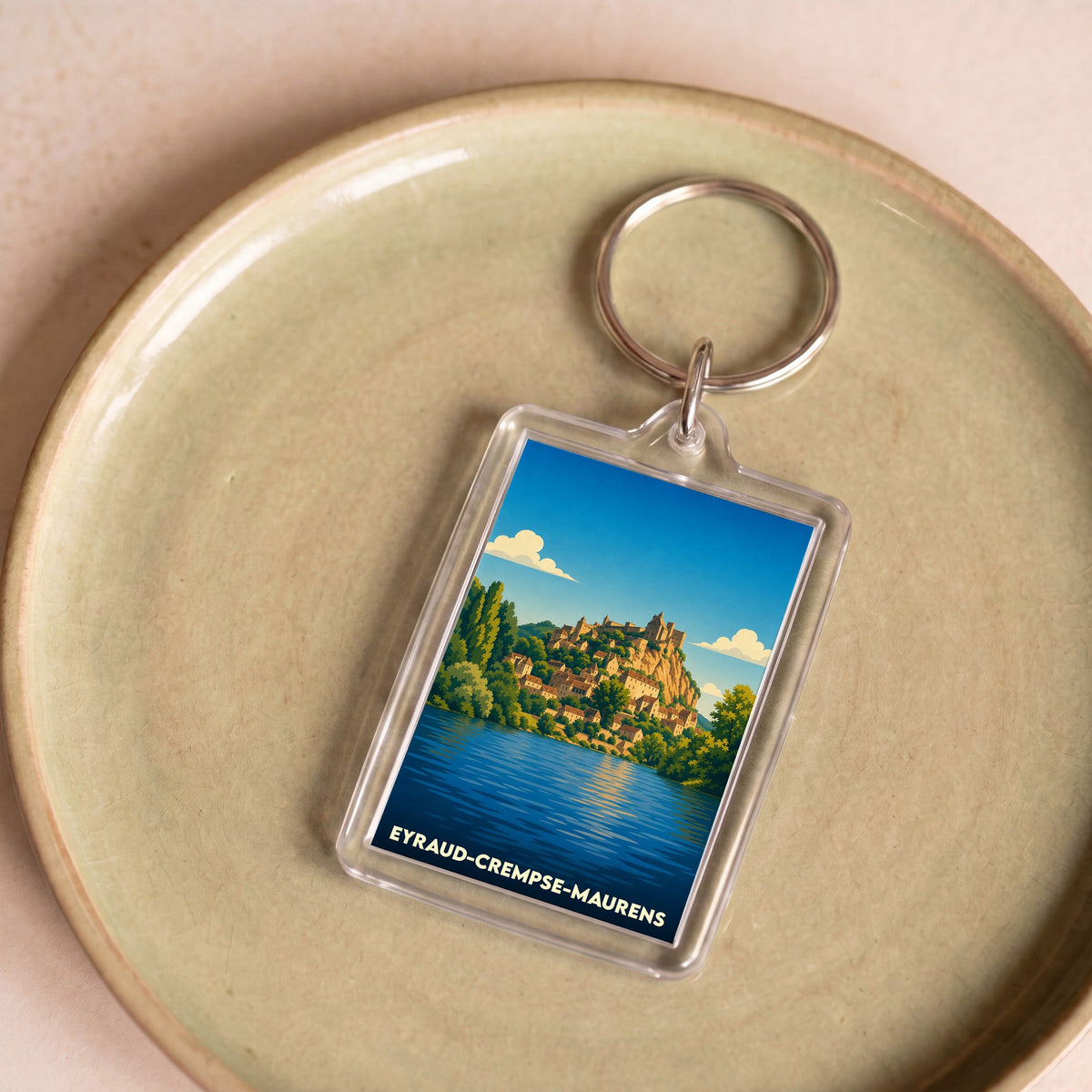 Porte-clés souvenir de la ville d'Eyraud-Crempse-Maurens avec une illustration stylisée d'un village médiéval au bord de l'eau.