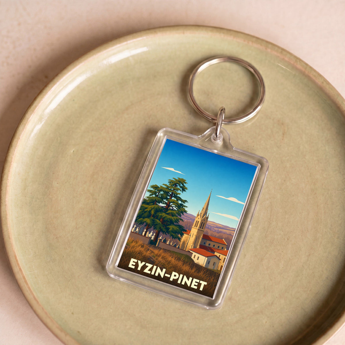 Porte-clés souvenir de la ville d'Eyzin-Pinet avec une illustration stylisée de son église et de son paysage.