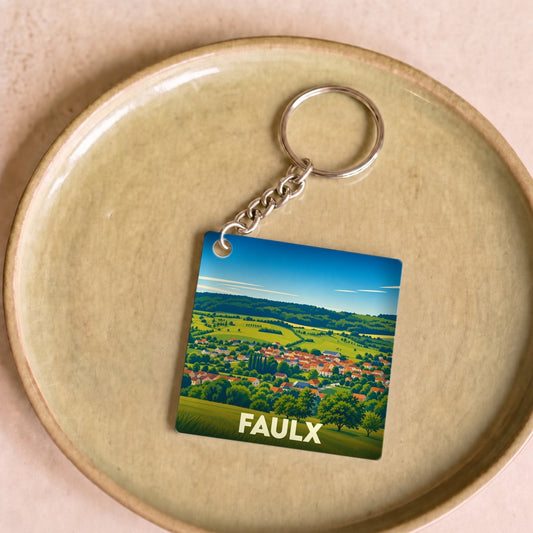 Porte-clés souvenir de la ville de Faulx avec une illustration stylisée de son paysage champêtre.