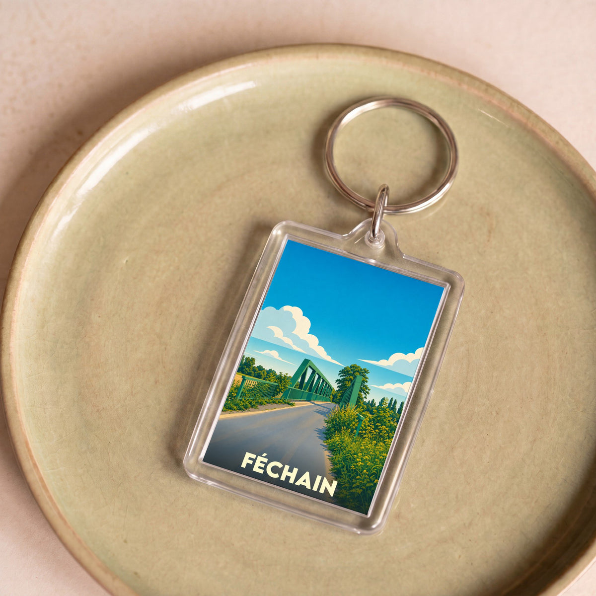 Porte-clés souvenir de la ville de Féchain avec une illustration stylisée d'un pont vert sous un ciel bleu.