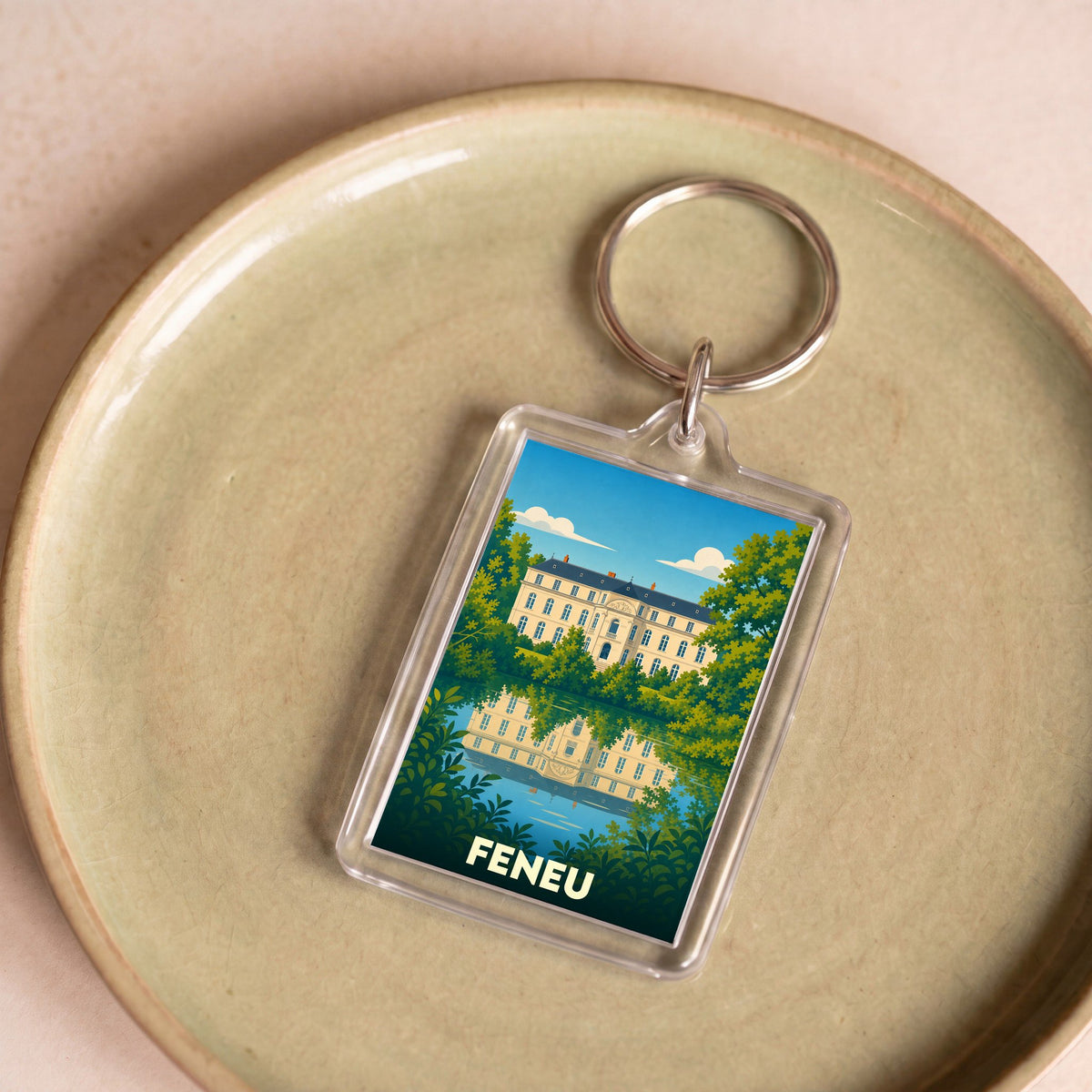 Porte-clés souvenir de la ville de Feneu avec une illustration stylisée d'un château se reflétant dans l'eau.