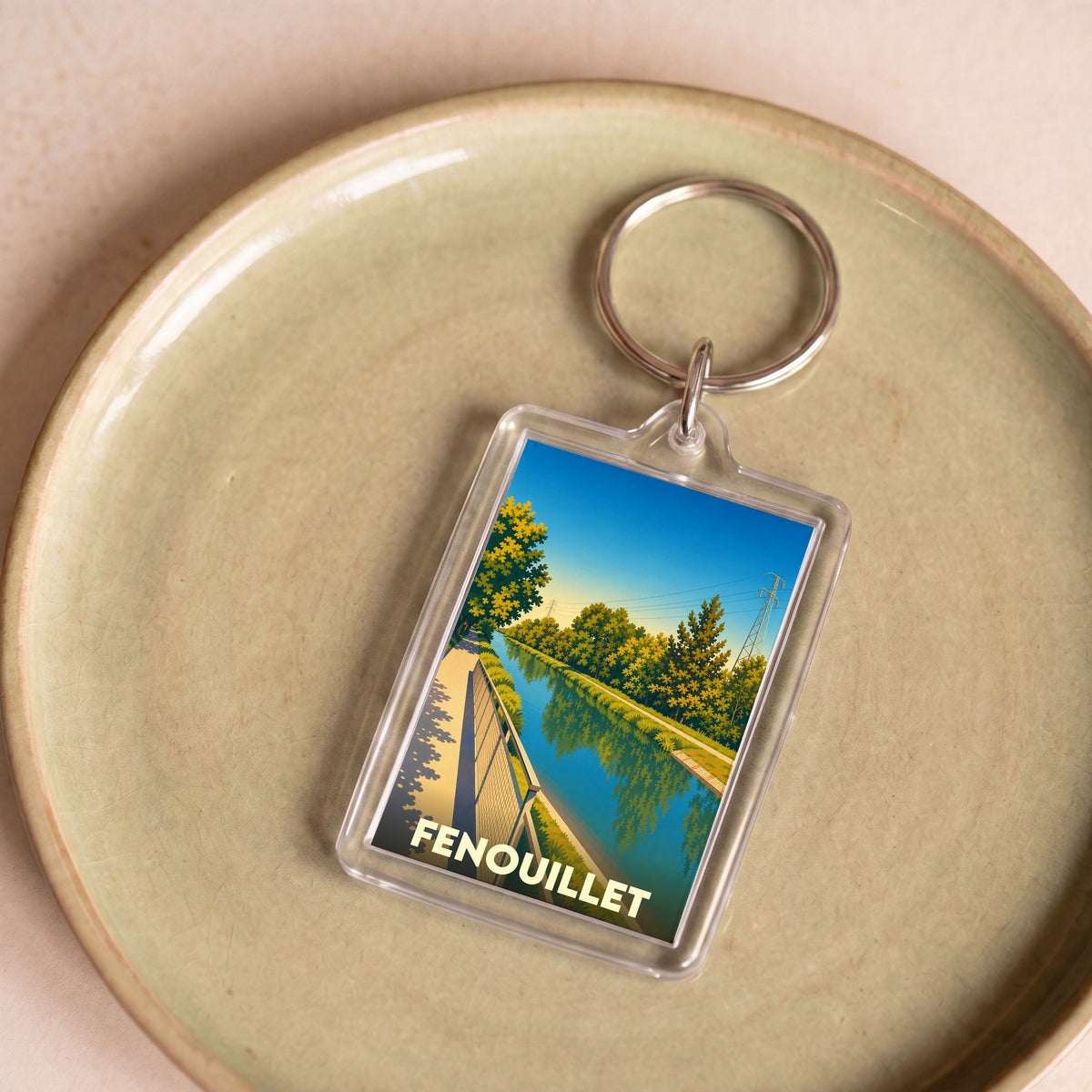 Porte-clés souvenir de la ville de Fenouillet avec une illustration stylisée d'un canal bordé d'arbres.