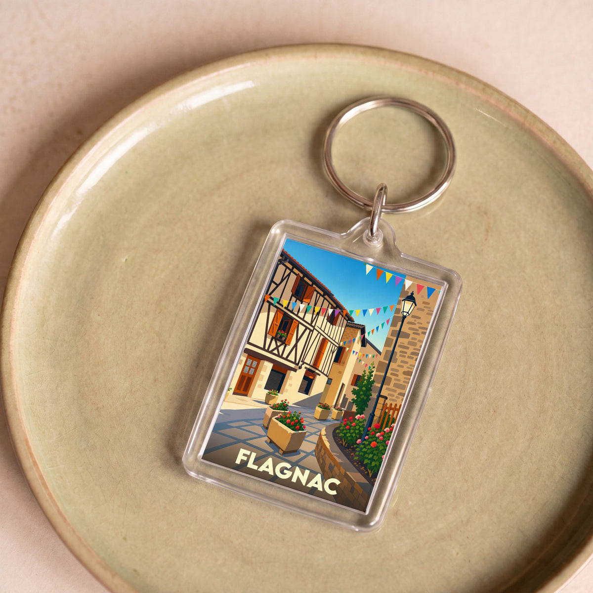 Porte-clés souvenir de la ville de Flagnac avec une illustration stylisée d'une rue pittoresque.