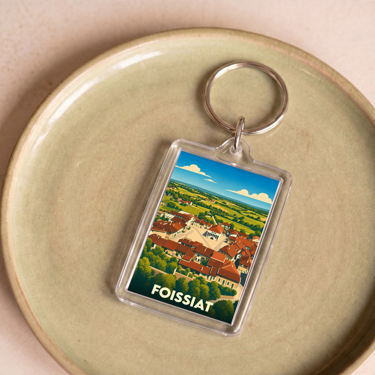 Porte-clés souvenir de la ville de Foissiat avec une illustration stylisée d'un paysage de village.