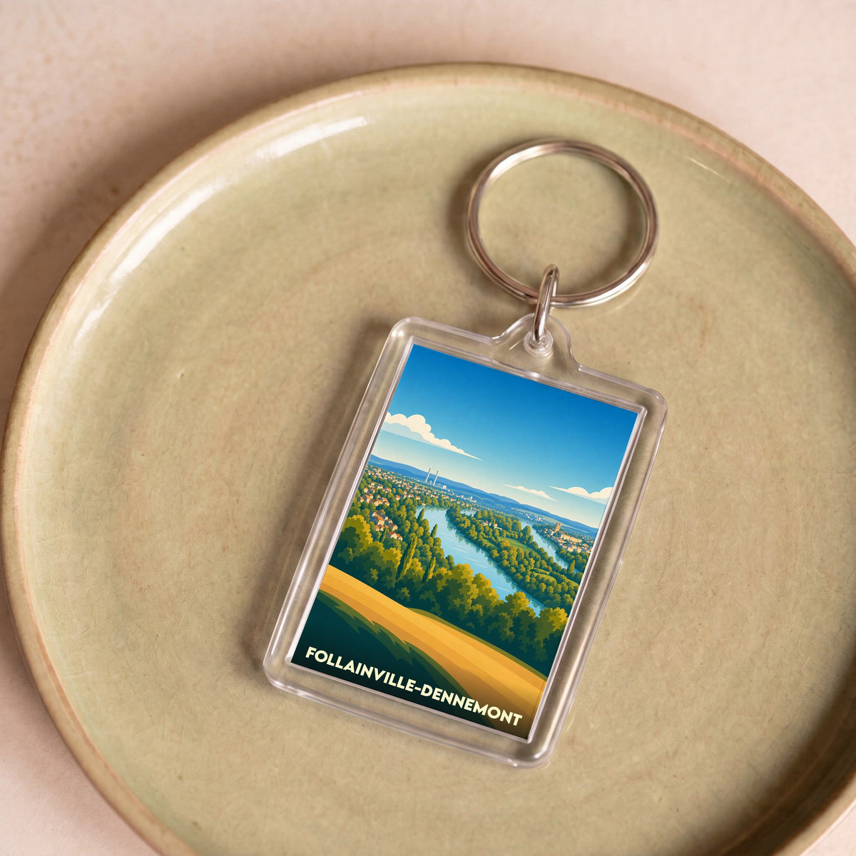 Porte-clés souvenir de la ville de Follainville-Dennemont avec une illustration paysagère stylisée.