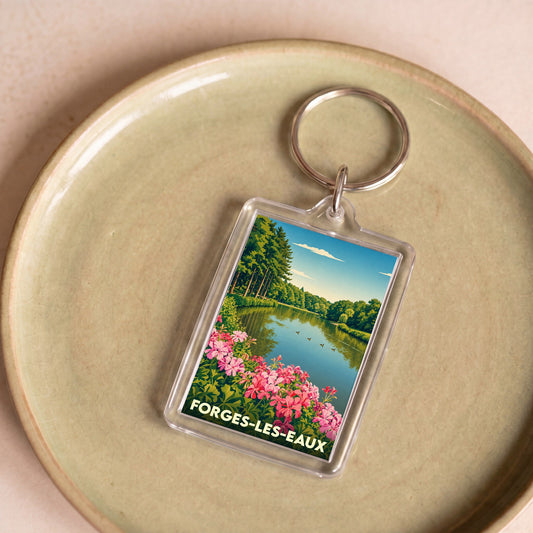Porte-clés souvenir de Forges-les-Eaux avec une illustration bucolique d'un lac bordé de fleurs.