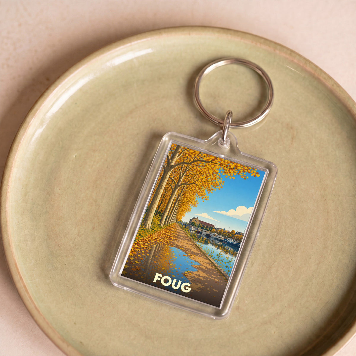 Porte-clés souvenir de la ville de Foug avec une illustration automnale stylisée d'un canal bordé d'arbres.