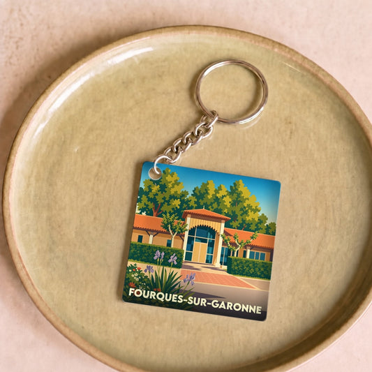 Porte-clés souvenir de Fourques-sur-Garonne avec une illustration stylisée du village dans un cadre transparent.