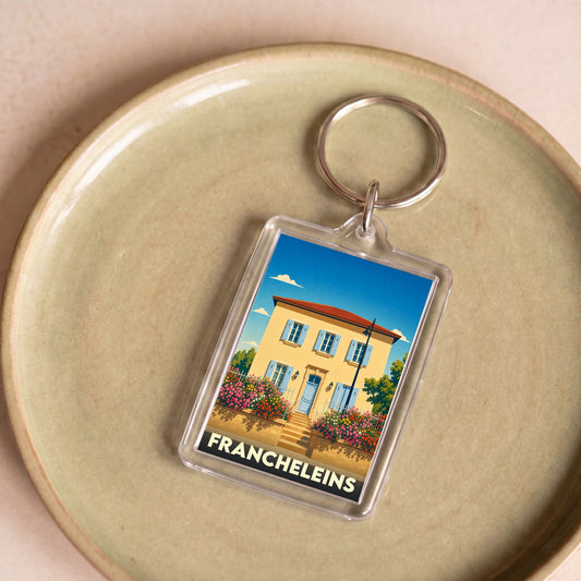 Porte-clés souvenir de la ville de Francheleins avec une illustration stylisée d'une maison ensoleillée.